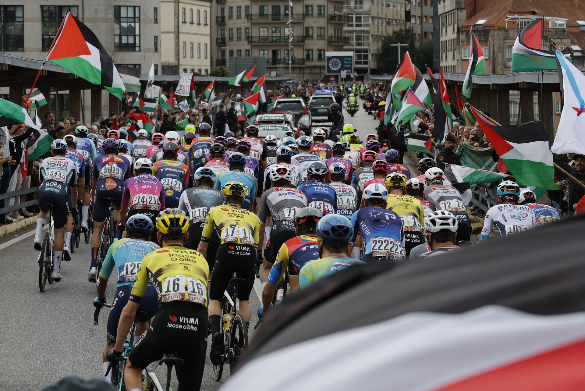-El pelotón pasa ante las personas concentradas en protesta por la situación de Gaza , al inicio de la etapa 16 de la Vuelta Ciclista a España que se disputa este martes entre Poio y Mos-Castro de Herville (Pontevedra), de 167.9 km de recorrido. EFE/Lavandeira