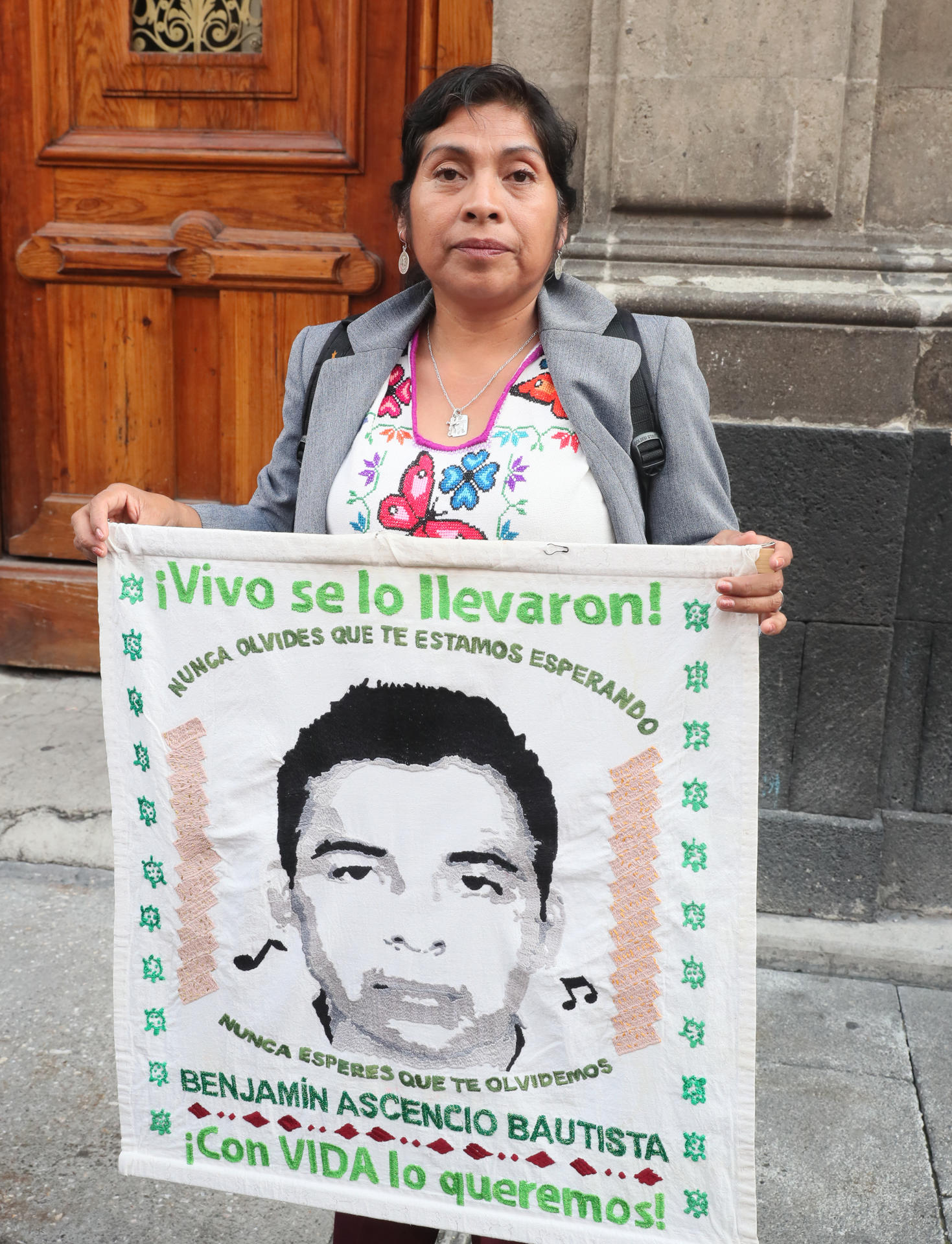 Una mujer sostiene la imagen de uno de los 43 de Ayotzinapa, a su salida del Palacio Nacional después de reunión con la presidenta de México, Claudia Sheinbaum este jueves, en Ciudad de México (México). EFE/Mario Guzmán