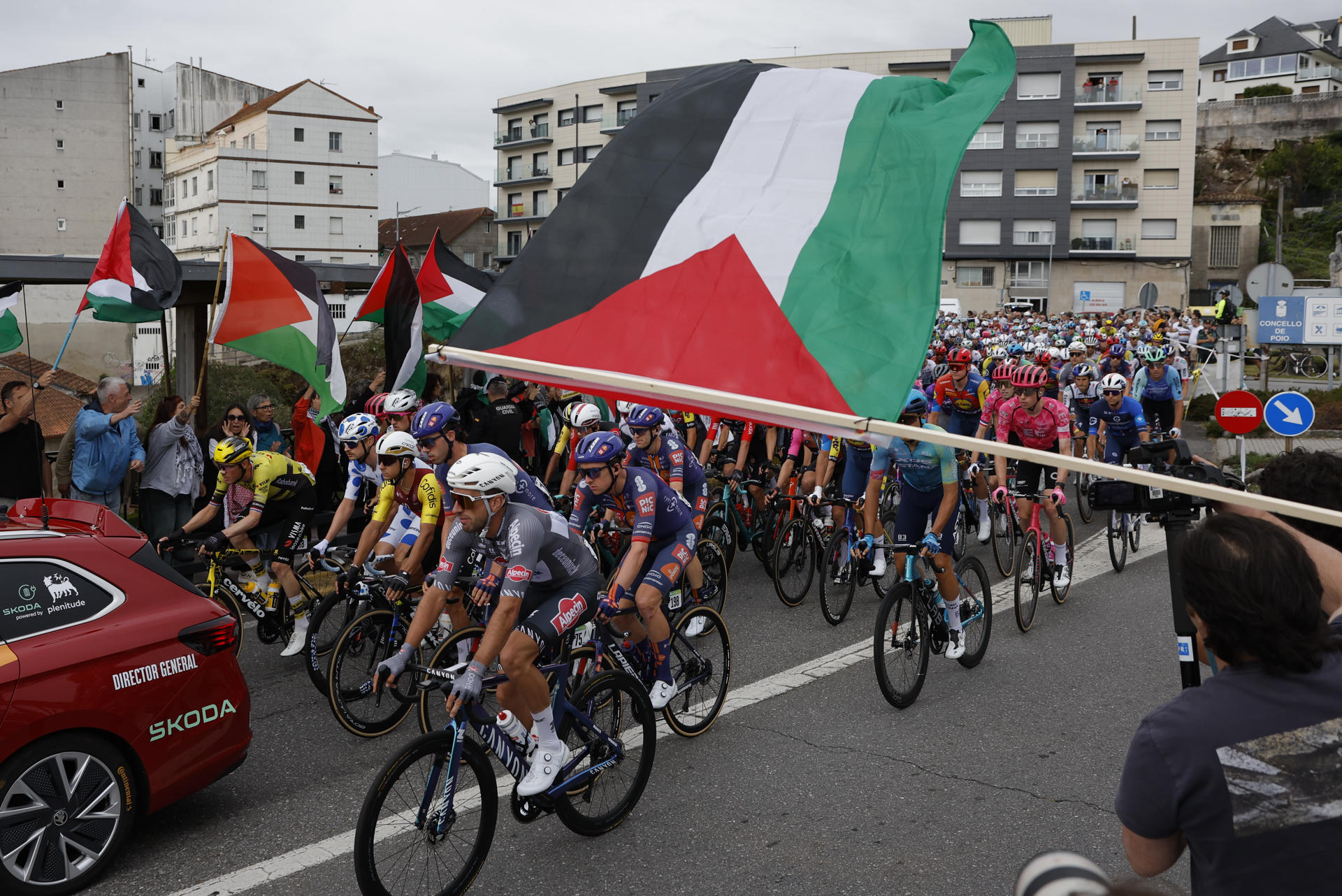 Los ciclistas pasan ante las protestas propalestina durante la etapa 16 de la Vuelta Ciclista a España que se disputa este martes entre Poio y Mos-Castro de Herville (Pontevedra), de 167.9 km de recorrido. EFE/ Lavandeira Jr