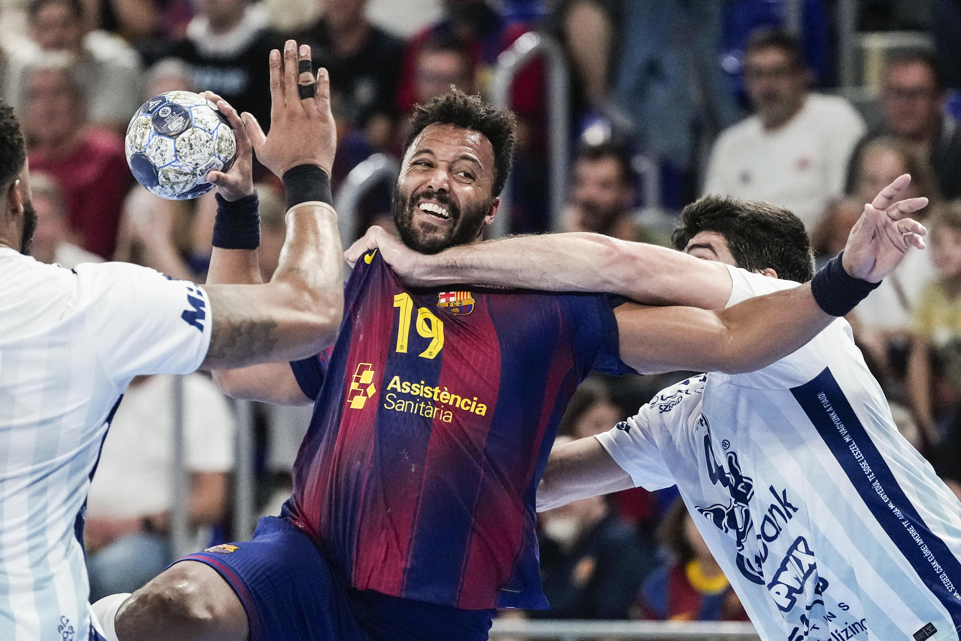 El lateral del Barça Timothey N'Guessan (c) lanza a puerta defendido por Imanol Garciandía (d), del OTP Bank, durante el partido correspondiente a la temporada regular de la Liga de Campeones de Balonmano que Barça y OTP Bank-Pick Szeged disputan hoy jueves en el Palau Blaugrana. EFE/ Enric Fontcuberta.