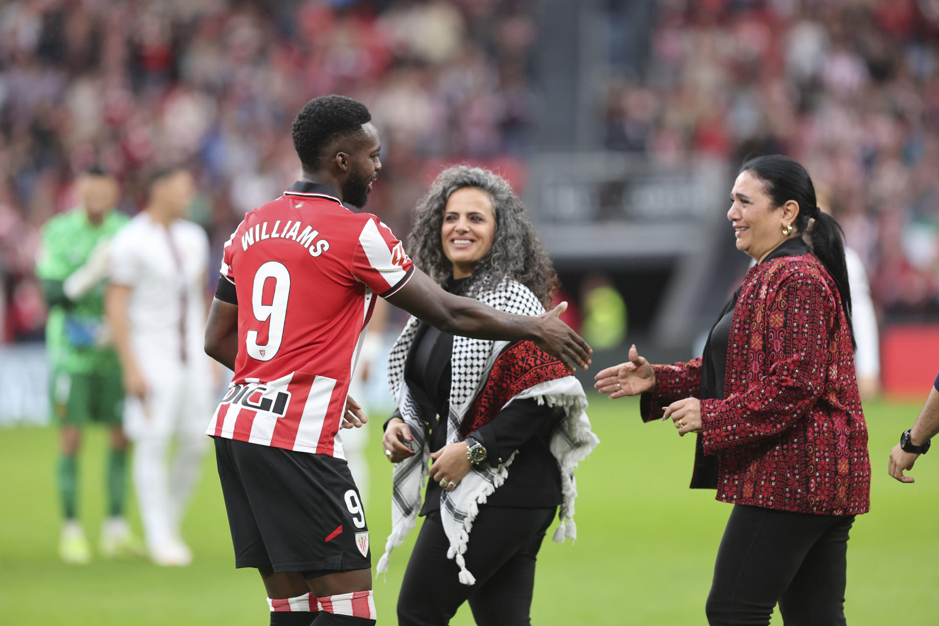 El delantero del Athletic Club Iñaki Williams, saluda a dos mujeres palestinas, durante el partido de la jornada 8 de LaLiga EA Sports entre el Athletic Club y el Mallorca, este sábado en el estadio de San Mamés en Bilbao.-EFE/ Luis Tejido
