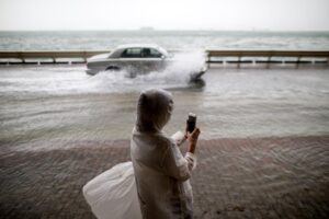 Una mujer toma fotos al paso de coches por una calle inundada durante el paso de un tifóen Hong Kong (China), en una imagen de archivo. EFE/Jerome Favre