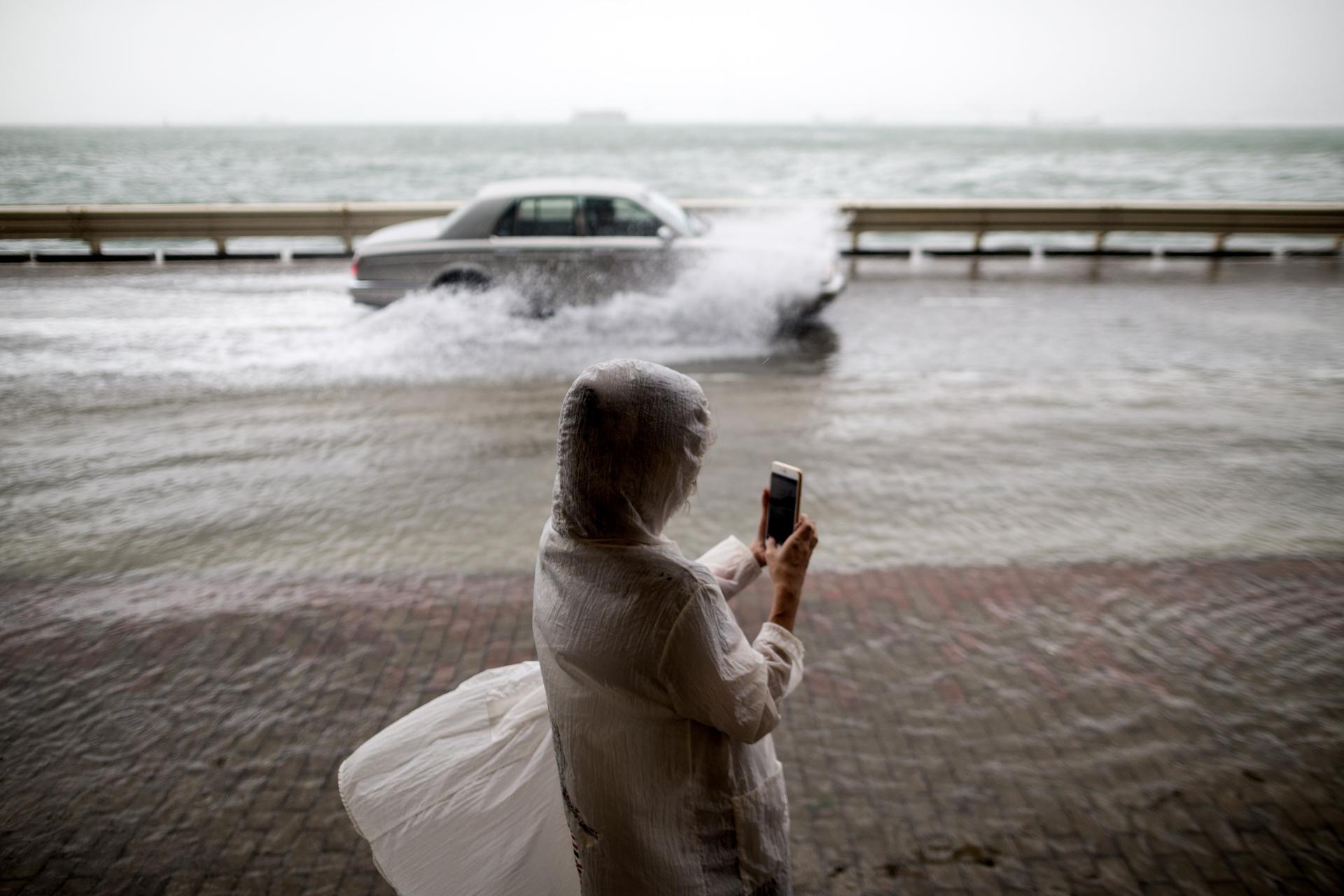 Una mujer toma fotos al paso de coches por una calle inundada durante el paso de un tifóen Hong Kong (China), en una imagen de archivo. EFE/Jerome Favre