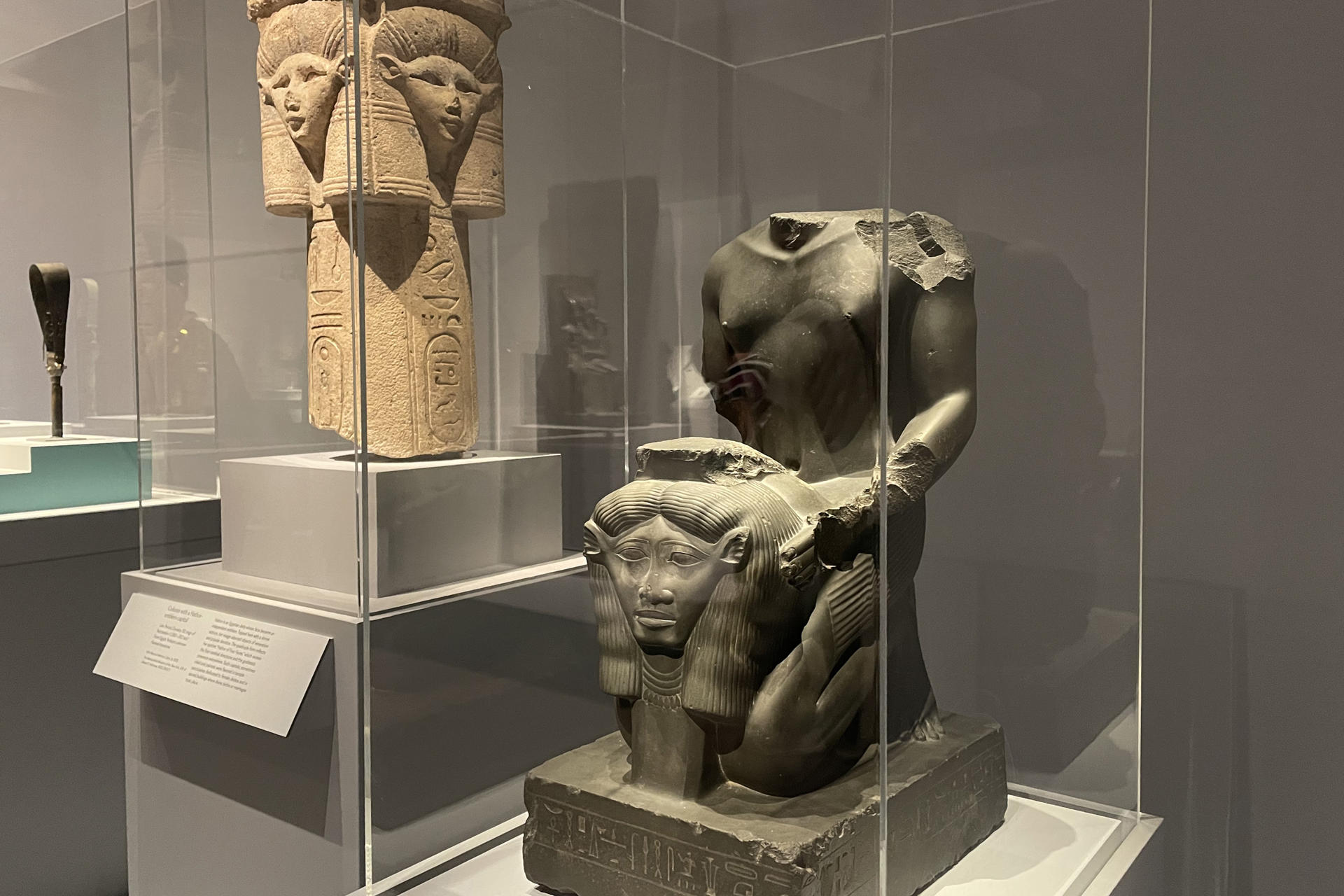 Fotografía que muestra una estatua de Amenemopetemhat arrodillado y sosteniendo el emblema de Hathor (d) junto a una columna con capitel con el emblema de Hathor durante la exposición 'Divine Egypt' ('Egipto divino') este lunes, en el Museo Metropolitano (Met), en Nueva York (Estados Uninos). EFE/ Alicia Sánchez
