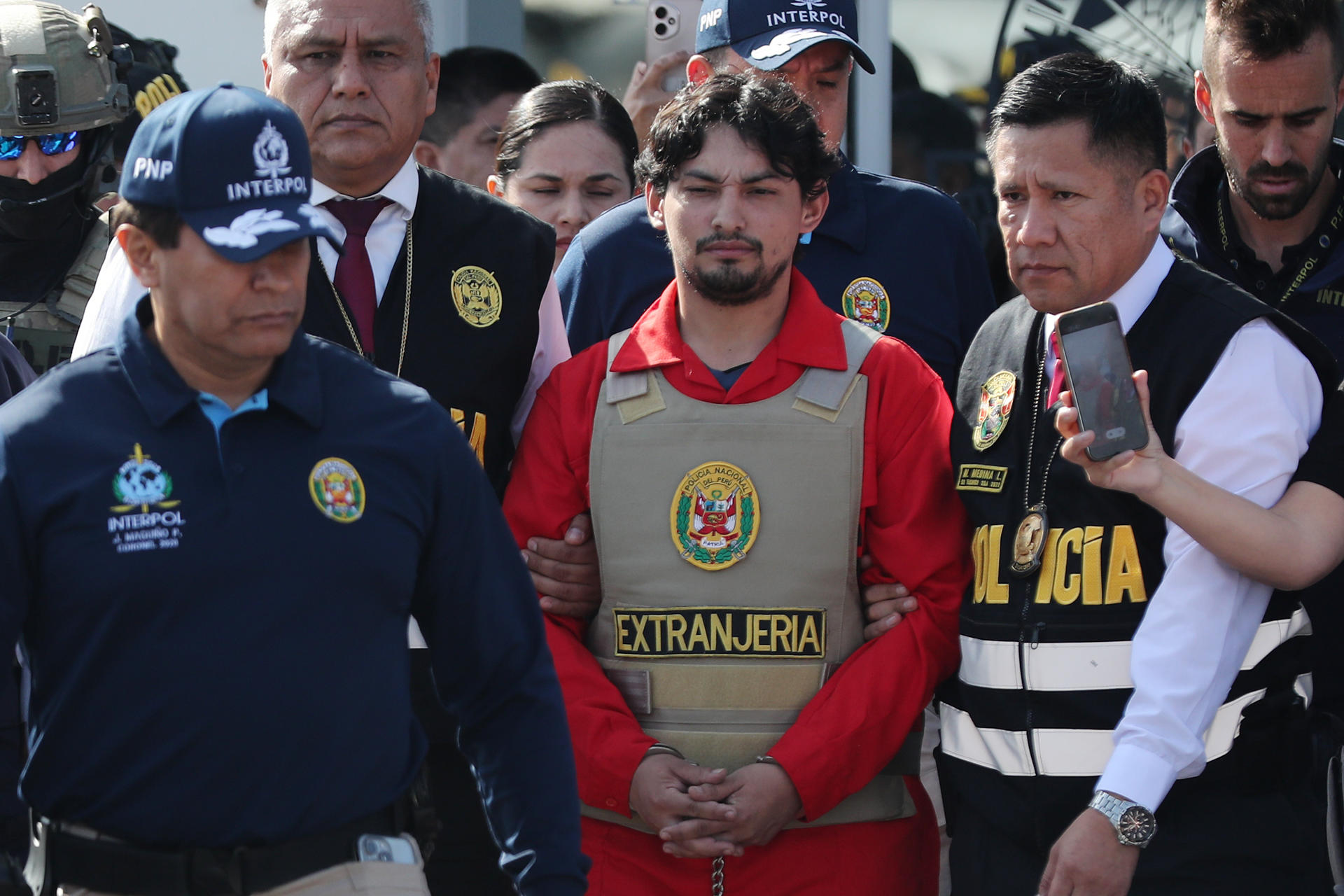 Matías Agustín Ozorio (c), de nacionalidad argentina, es trasladado por integrantes de la Policía Nacional de Perú (PNP) y de Interpol para ser entregado a la Policía Argentina este jueves, en la Base Aérea de Policía Aérea de Perú en Lima (Perú). EFE/ Paolo Aguilar
