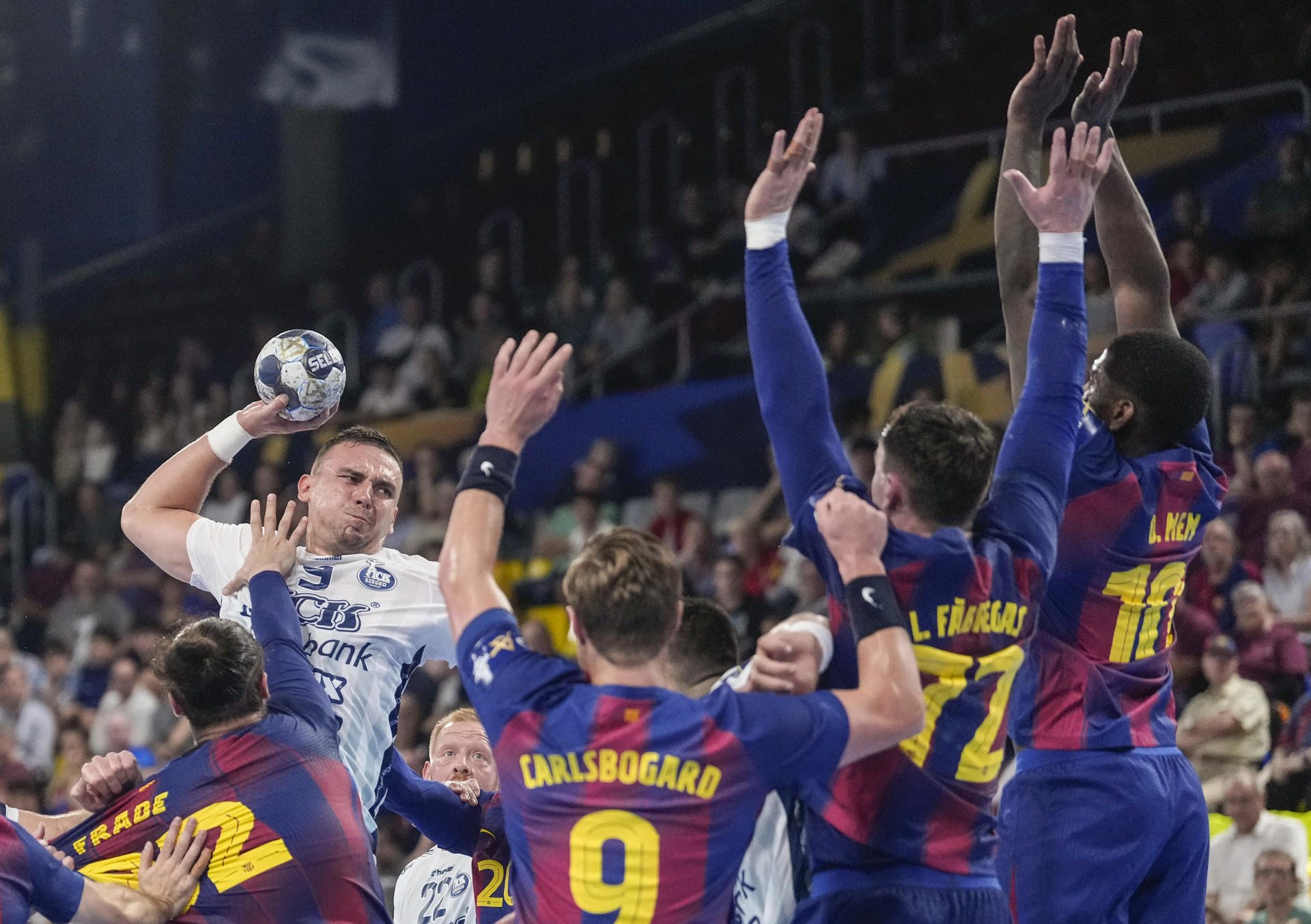 El extremo del OPT Bank Bodo Richard (i) intenta lanzar ante los jugadores del Barça, durante el partido correspondiente a la temporada regular de la Liga de Campeones de Balonmano que Barça y OTP Bank-Pick Szeged disputan hoy jueves en el Palau Blaugrana. EFE/ Enric Fontcuberta.