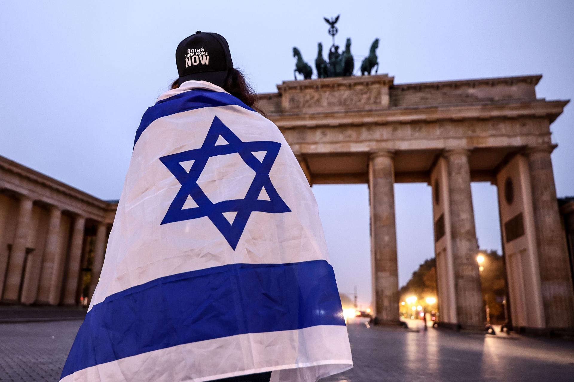 Una mujer envuelta en la bandera israelí asiste a una vigilia conmemorativa para conmemorar el segundo aniversario del ataque de Hamás contra Israel, frente a la Puerta de Brandeburgo en Berlín, Alemania, el 7 de octubre de 2025. EFE/EPA/FILIP SINGER
