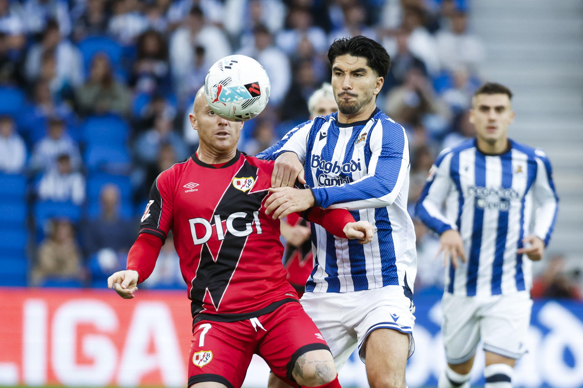 El centrocampista del Rayo Isi Palazón (i) pelea un balón con Carlos Soler (c), de la Real, durante el partido de LaLiga de fútbol que Real Sociedad y Rayo Vallecano disputan este domingo en el Real Arena, en San Sebastián. EFE/Jaun Herrero
