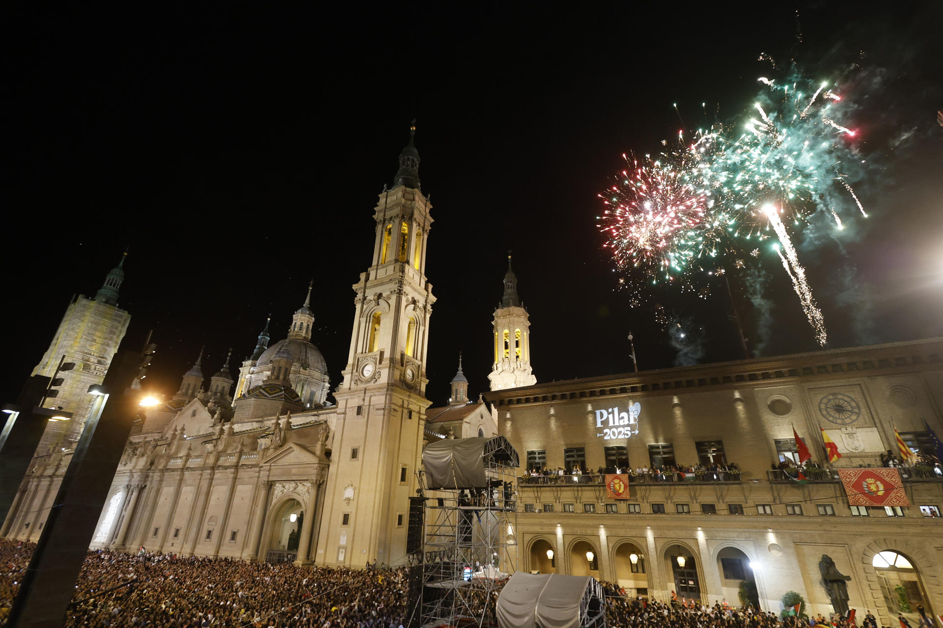 Vista general de la lectura del pregón de inicio de las Fiestas del Pilar 2025 a cargo de los cineastas zaragozanos Javier Macipe, Pilar Palomero y Paula Ortiz, acompañados por la diseñadora de vestuario Arantxa Ezquerro, la realizadora Blanca Torres y el actor Pepe Lorente, y la alcaldesa Natalia Chueca, este sábado en la plaza del Pilar en Zaragoza.-  EFE/ Javier Belver
